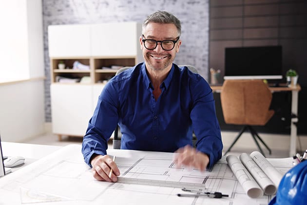 picture of man smiling at camera and working at desk with blueprints on it